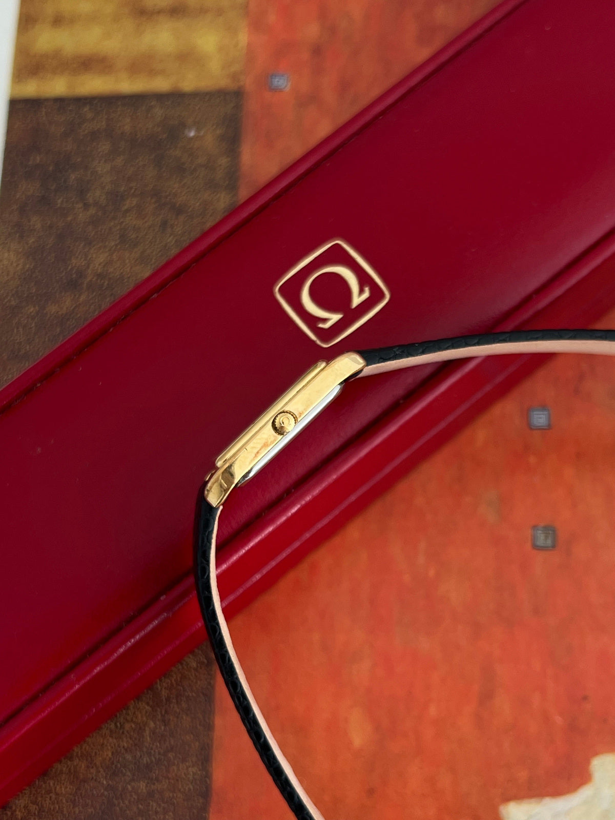 Side profile of the slim Omega De Ville gold tone case showing its Omega signed crown and new black aftermarket strap.