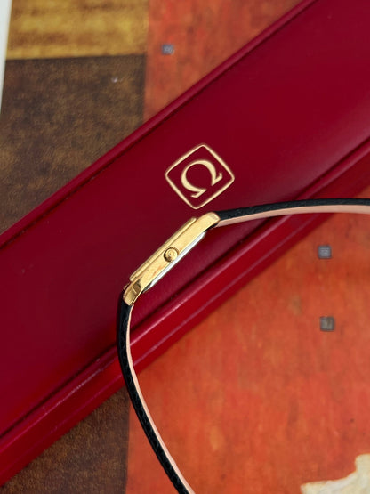 Side profile of the slim Omega De Ville gold tone case showing its Omega signed crown and new black aftermarket strap.