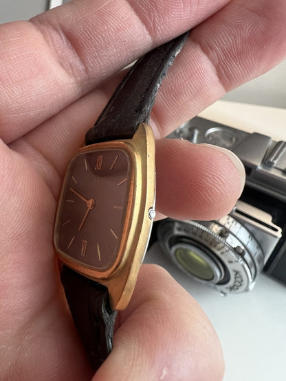 Side view of the Omega De Ville showing its integrated push button crown, slim gold tone case and black leather strap.