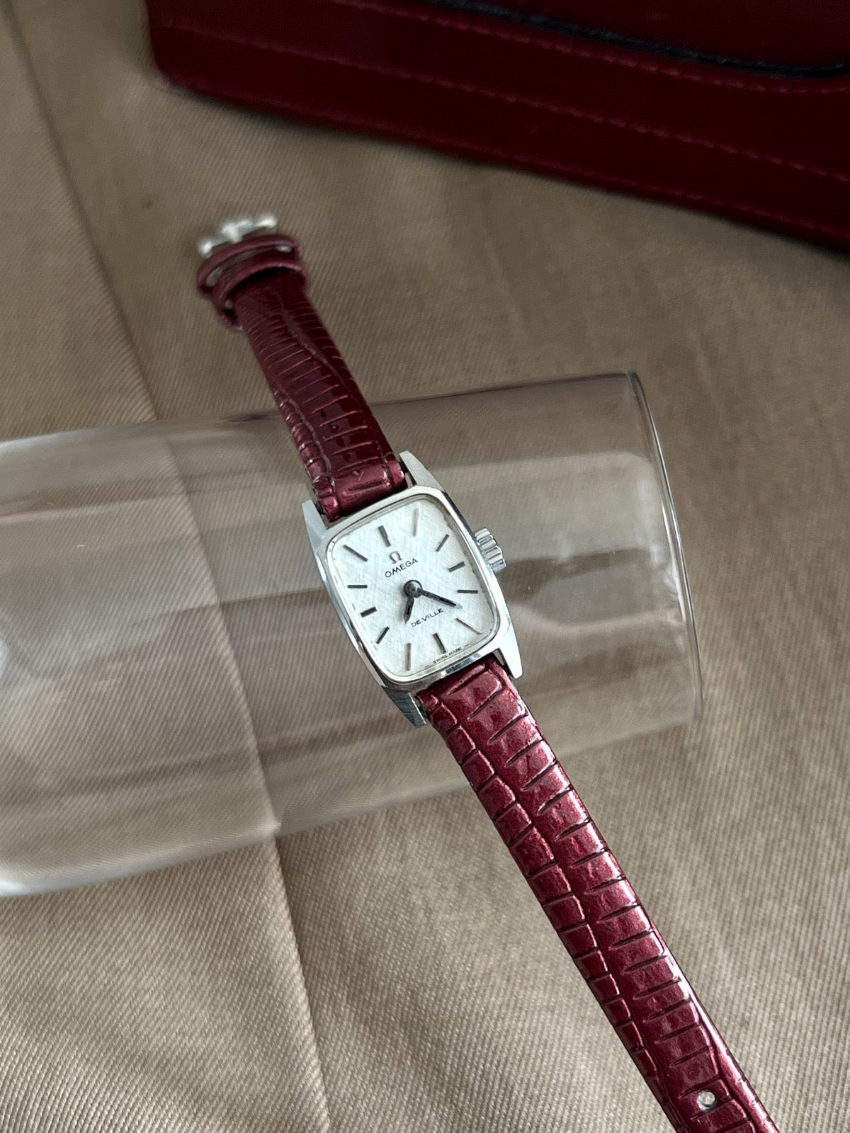 Close view of Omega De Ville silver linen dial, dark accented baton markers and burgundy leather strap