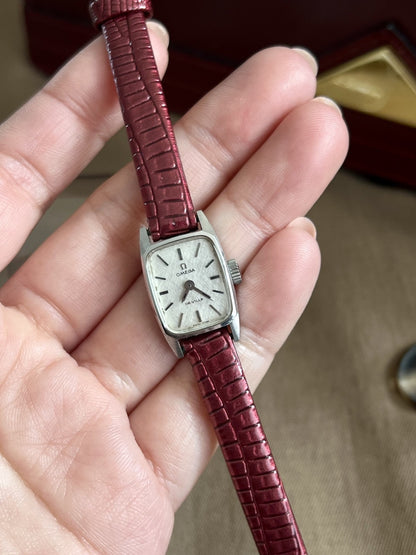 Omega De Ville petite rectangular watch held in hand showing the silver linen texture dial