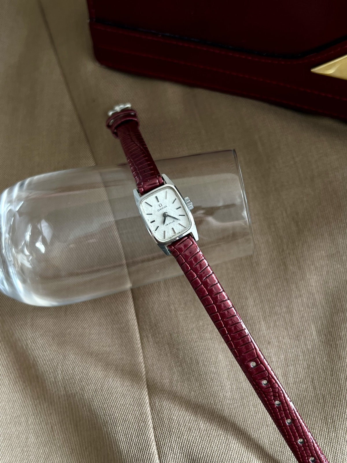 Omega De Ville silver linen dial watch on burgundy aftermarket leather strap beside a burgundy case