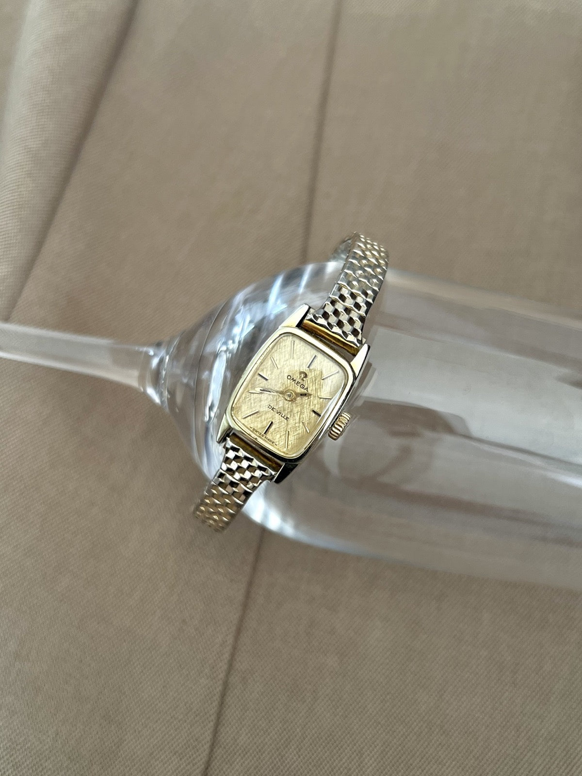 Angled front view of the Omega De Ville women’s watch with a gold linen dial and geometric two tone bracelet