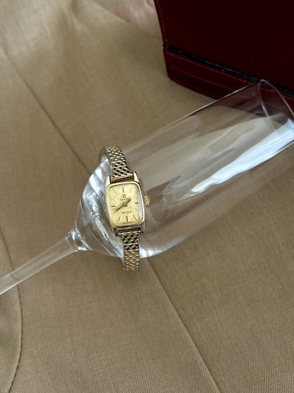 Full view of the Omega De Ville women’s watch and two tone elastic bracelet on a clear display stand