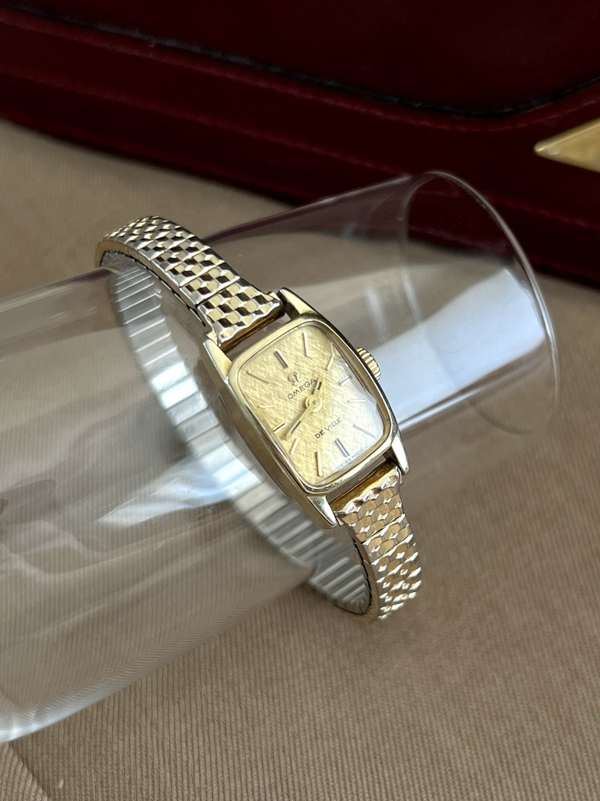 Omega De Ville women’s watch showing its rounded rectangular case, gold linen dial and two tone elastic bracelet
