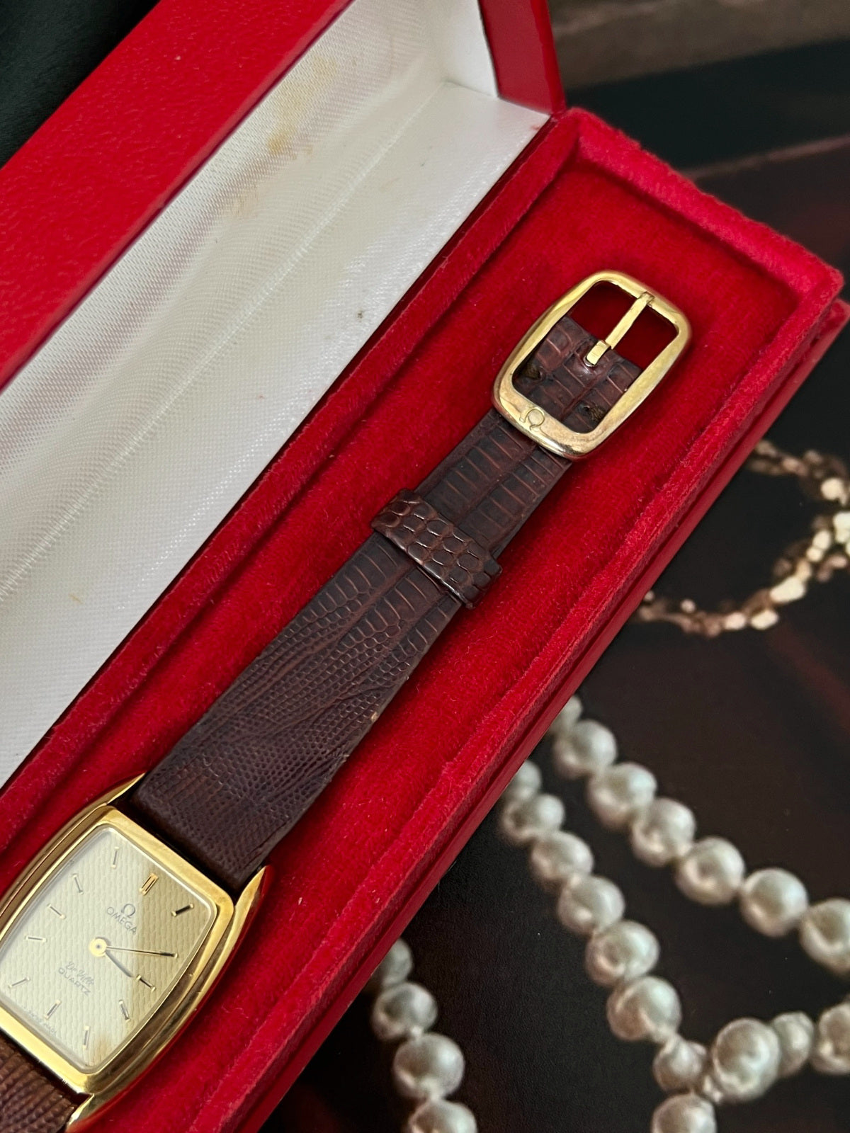 Original gold tone buckle and brown lizard strap beside the champagne dial of the Omega De Ville watch.