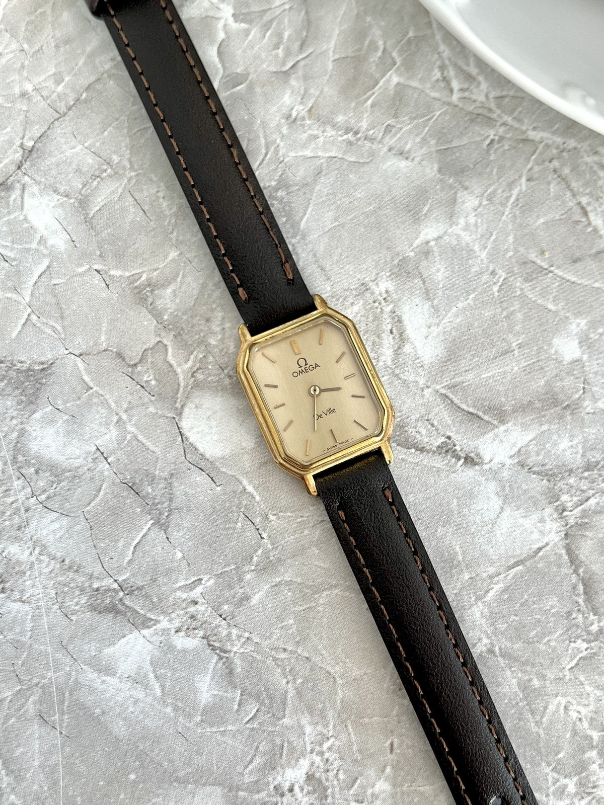 Three-quarter view of Omega De Ville rectangular women's watch with gold-tone case and baton dial