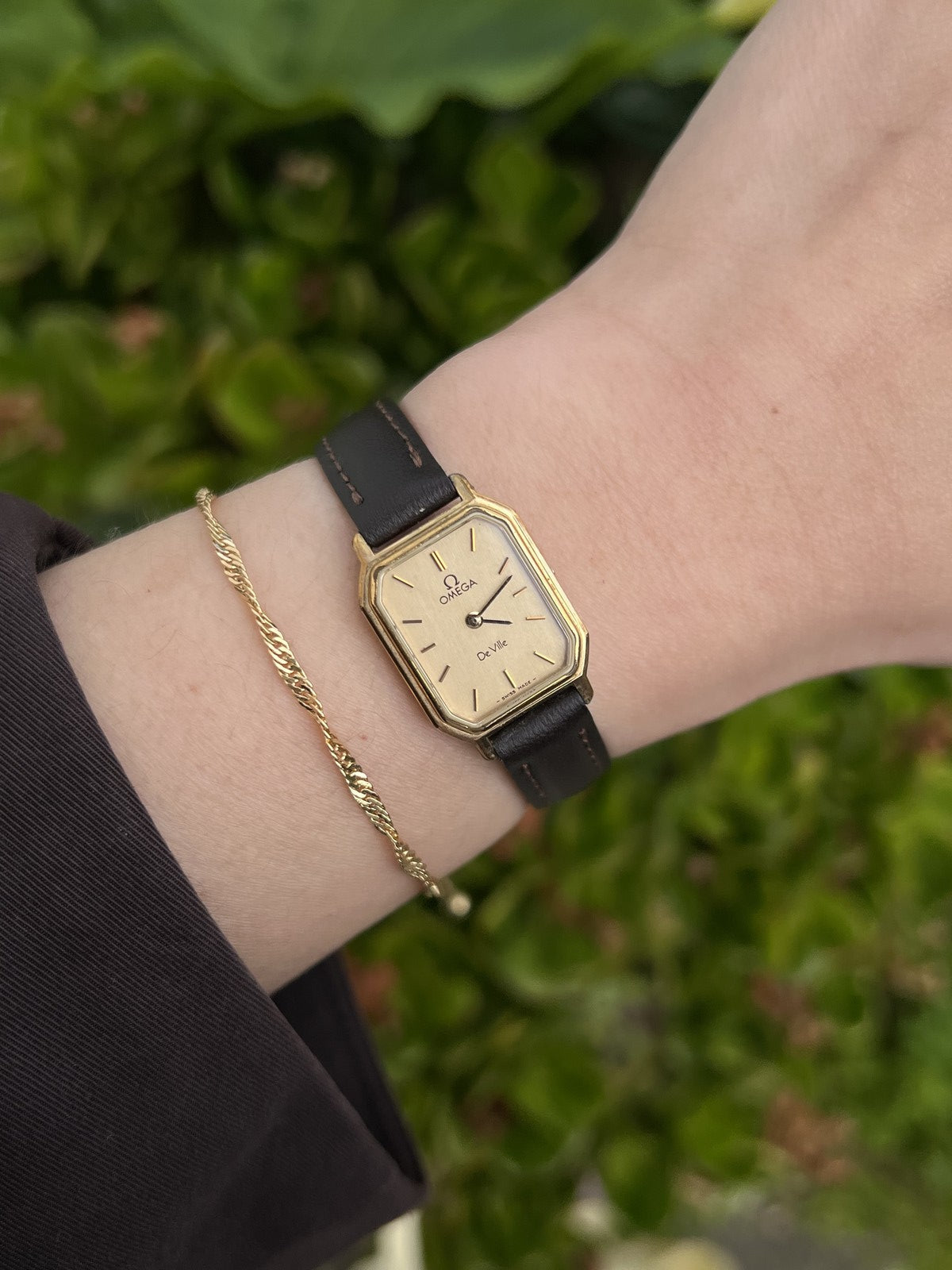 Omega De Ville rectangular champagne-dial women's watch in gold tone on a dark strap, worn on wrist