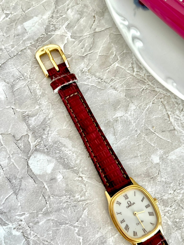 Red crocodile-pattern strap and gold-tone pin buckle on the Omega De Ville oval watch