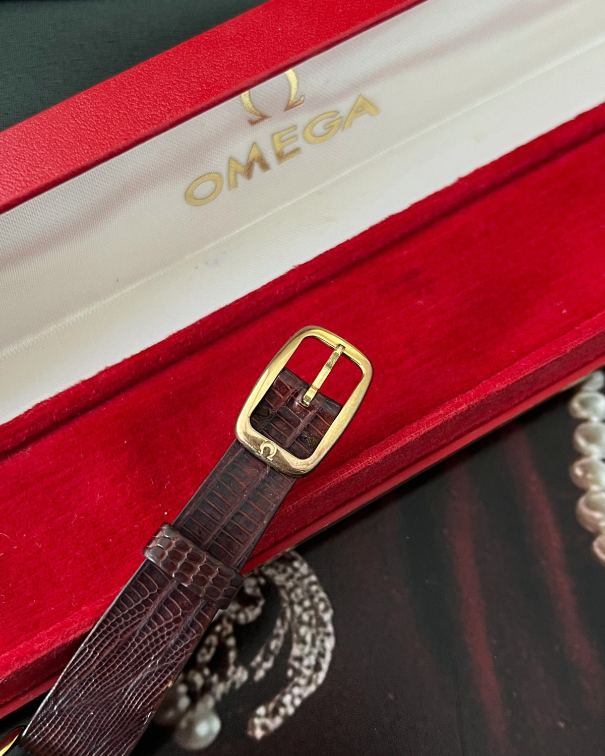 Close-up of the signed gold tone Omega buckle, brown lizard leather and Omega presentation box lining.
