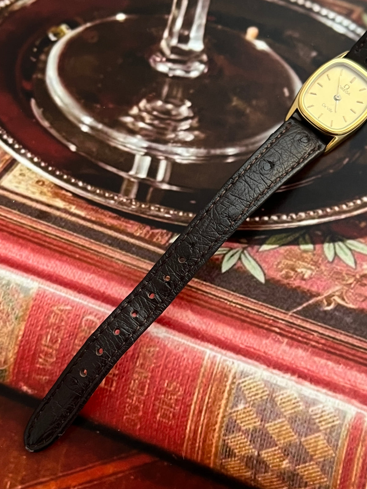 Omega De Ville small gold-tone cushion watch shown with its presentation box.