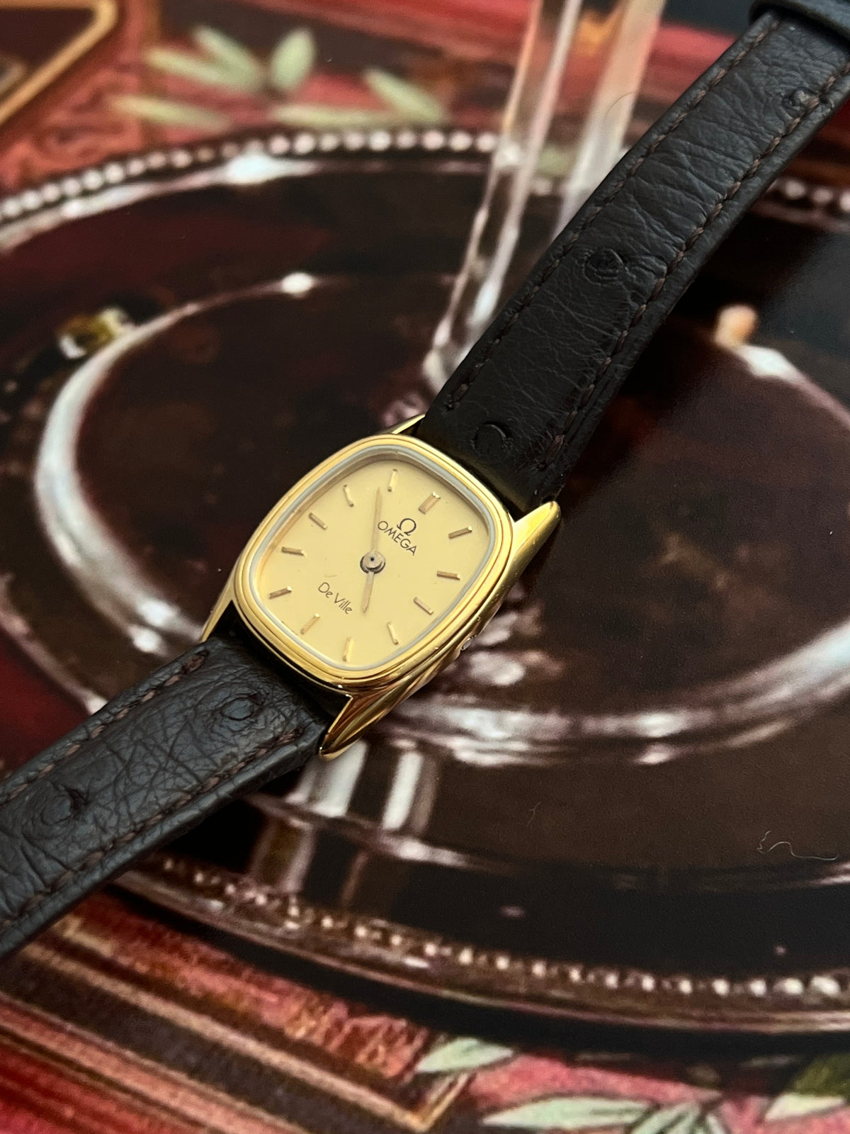 Omega De Ville petite cushion watch with champagne dial shown on the wrist.