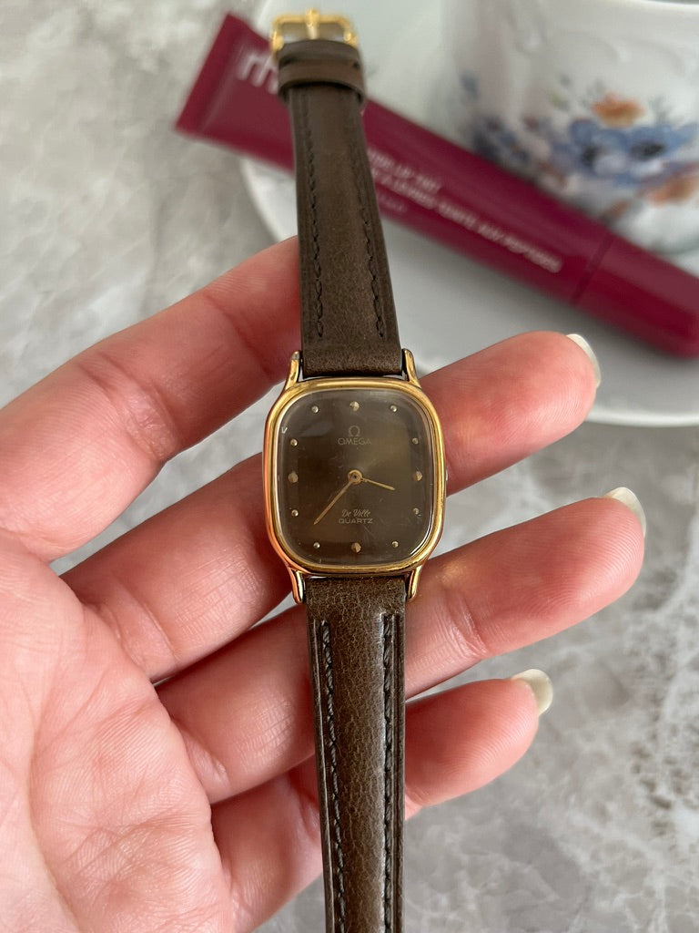 Omega De Ville quartz women's watch with smoked taupe dial, gold-tone cushion case and brown strap, front view