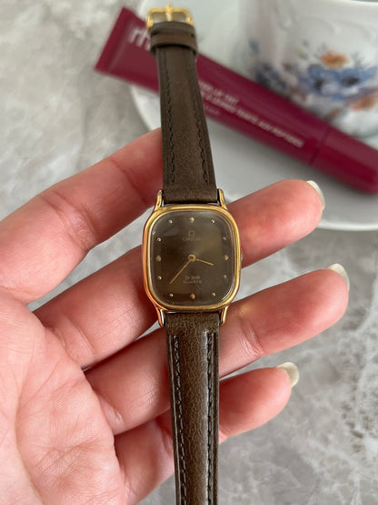 Omega De Ville quartz women's watch with smoked taupe dial, gold-tone cushion case and brown strap, front view