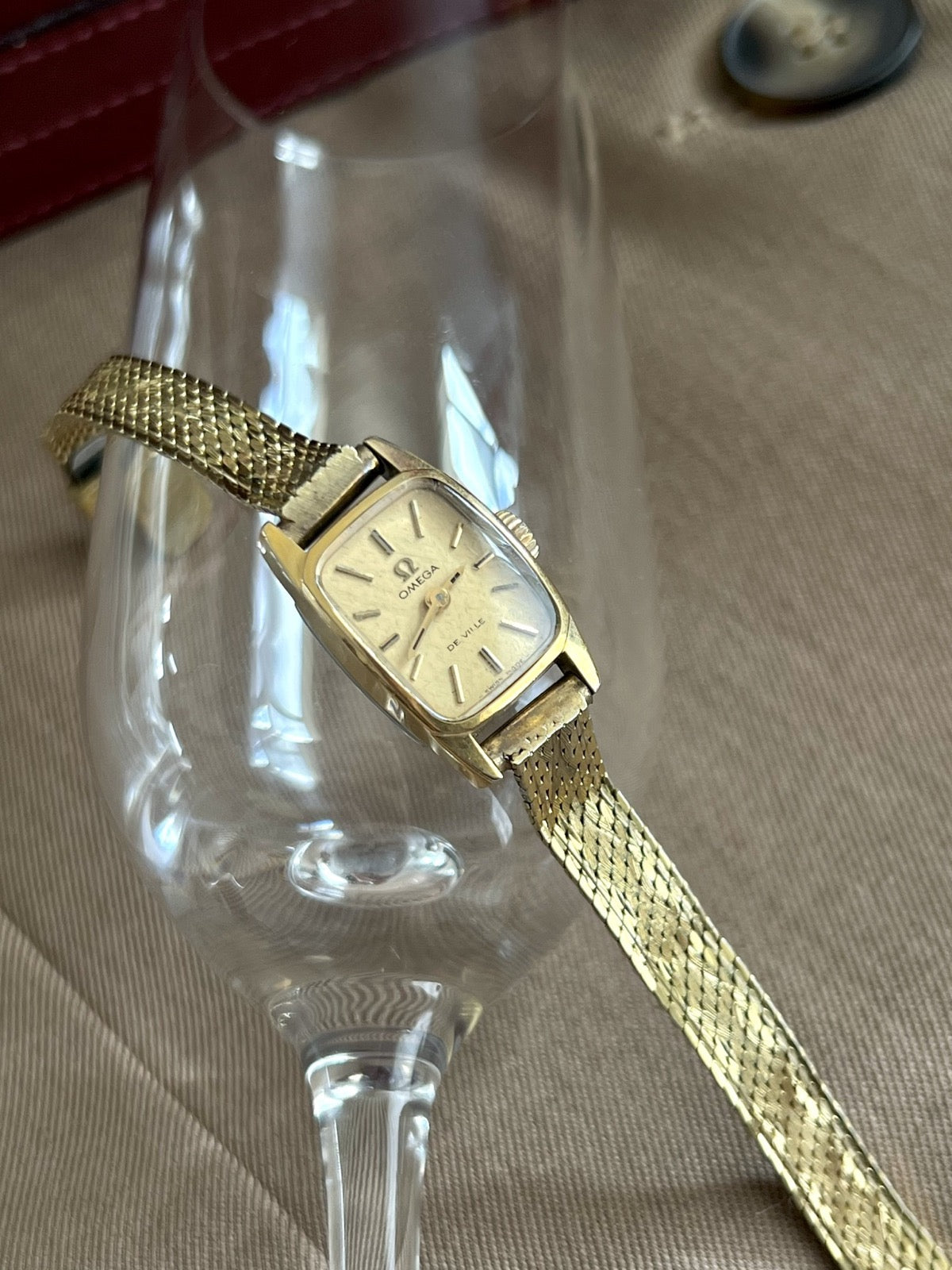 Angled view of the Omega De Ville women’s cocktail watch showing its rounded rectangular case and rolled gold woven bracelet