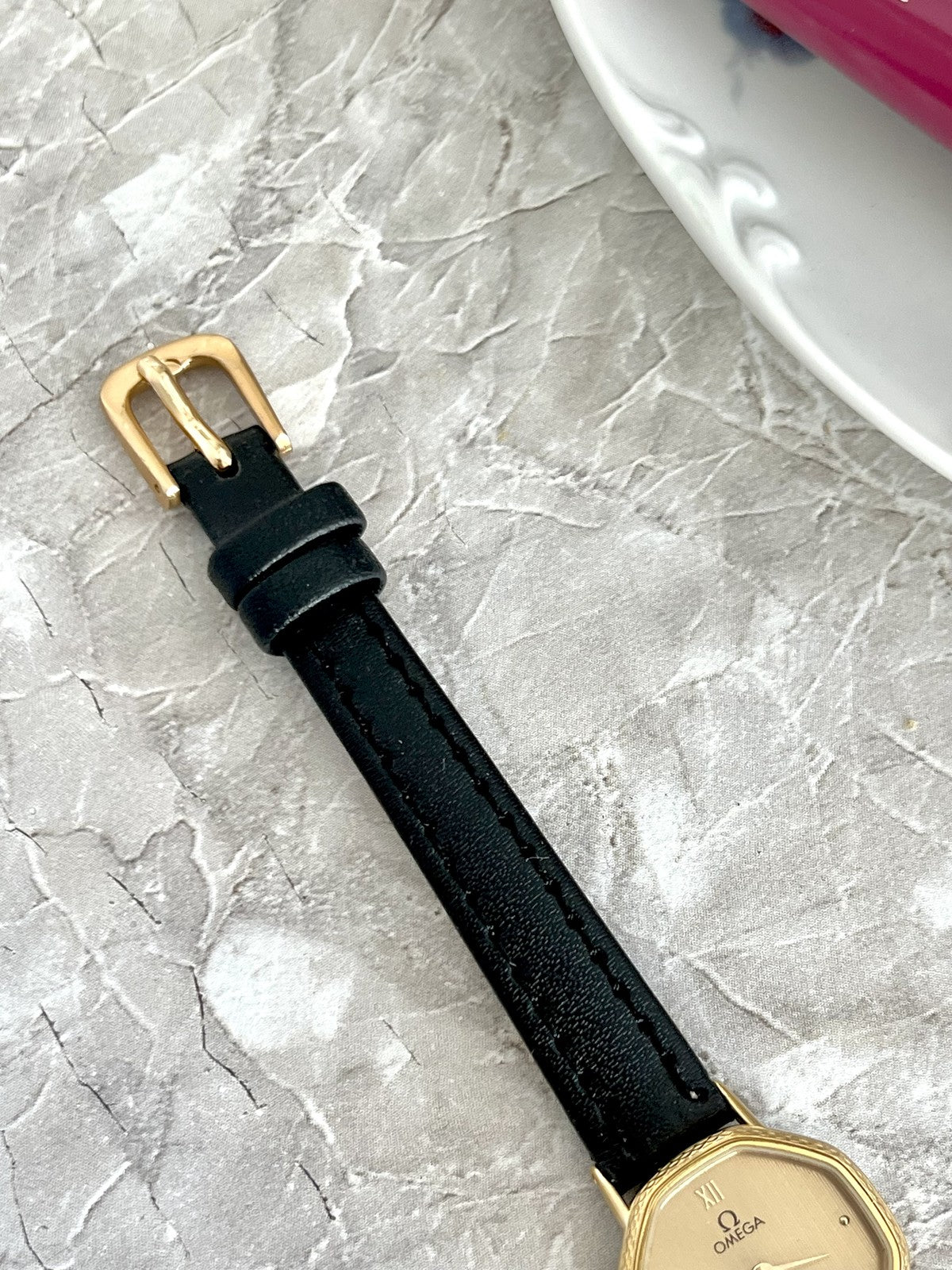 Dark stitched strap and gold-tone pin buckle on Omega De Ville rectangular women's watch