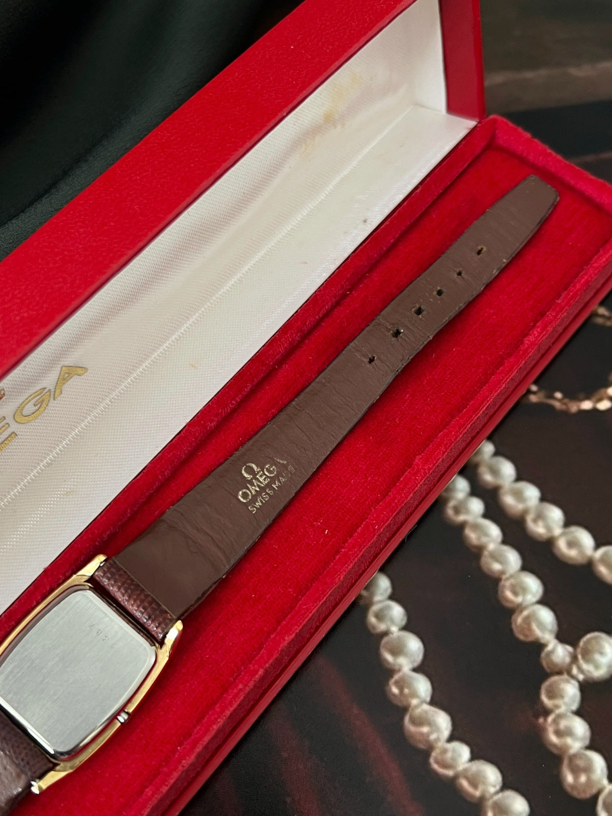 Reverse of the Omega De Ville tonneau watch showing the caseback and signed brown leather strap in its red box.