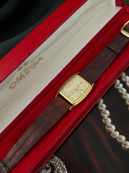 Omega De Ville wavy champagne dial and original brown lizard strap displayed diagonally in the red Omega box.