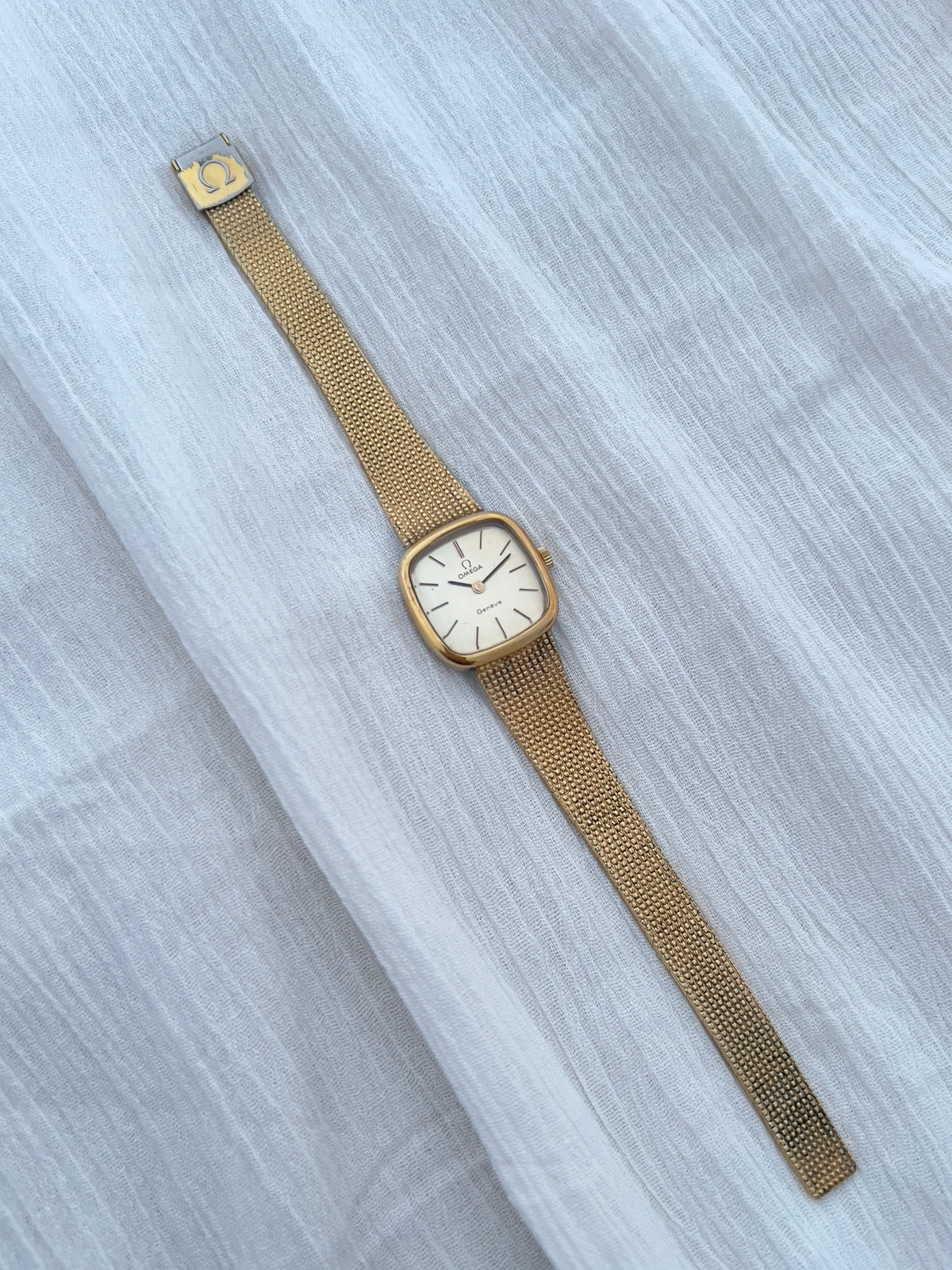 Wrist view showing the Omega Geneve's rounded-square gold-tone case and integrated mesh bracelet.