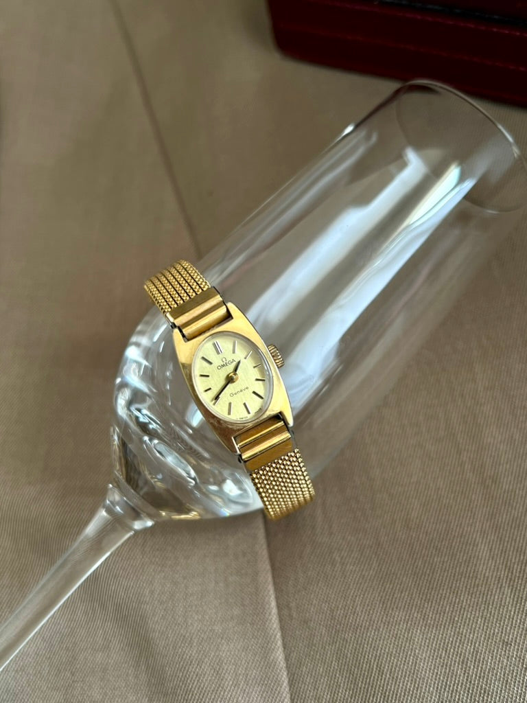 Front view of the Omega Geneve women’s watch with an oval dial, sculpted gold tone case and fine mesh bracelet