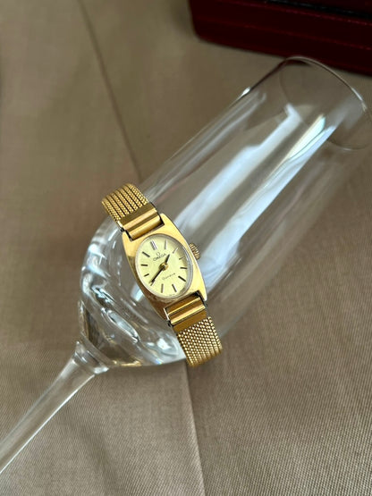 Front view of the Omega Geneve women’s watch with an oval dial, sculpted gold tone case and fine mesh bracelet