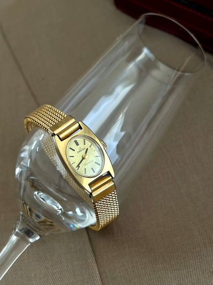Angled close view of the Omega Geneve women’s watch showing its oval champagne dial, baton markers and gold mesh bracelet