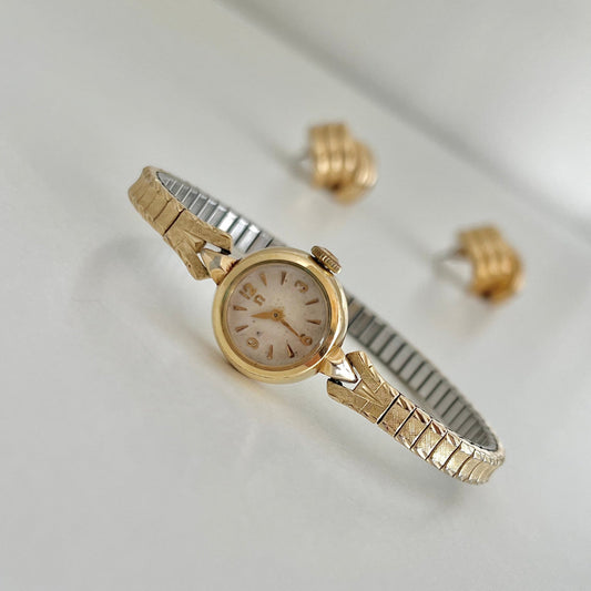Omega Gold Cocktail watch and earrings on a light gray background