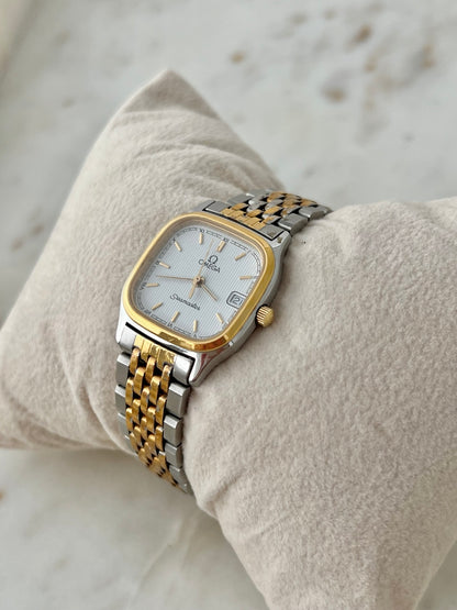 Close angled view of Omega Seamaster Brest two tone watch showing the white textured dial, gold tone bezel and date at three