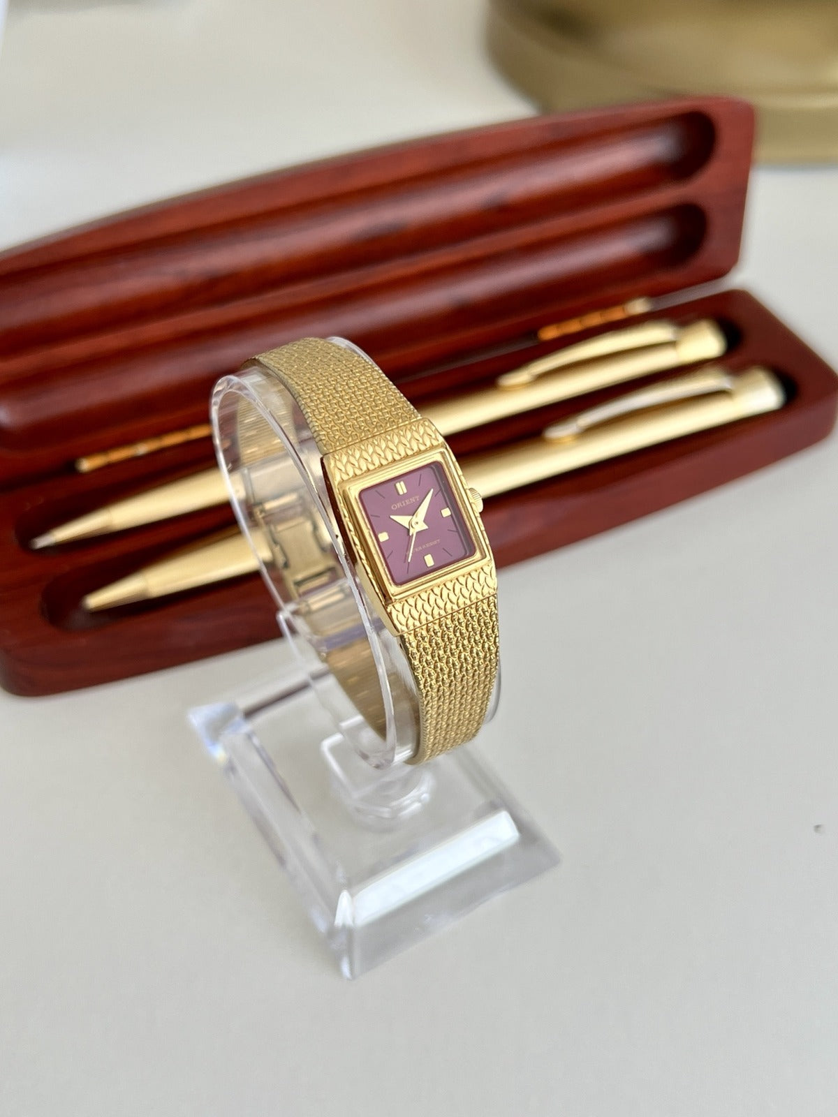 Angled view of the Orient burgundy dial women’s watch showing the slim gold tone case and woven bracelet.
