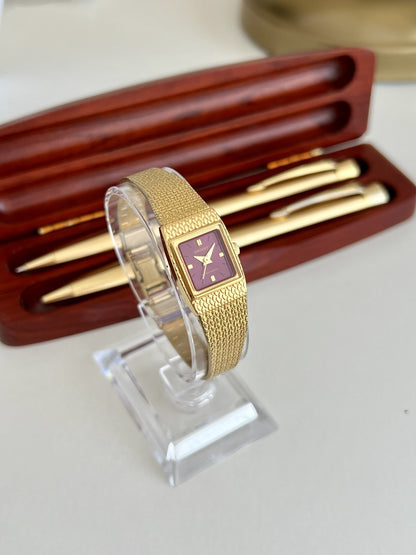 Angled view of the Orient burgundy dial women’s watch showing the slim gold tone case and woven bracelet.