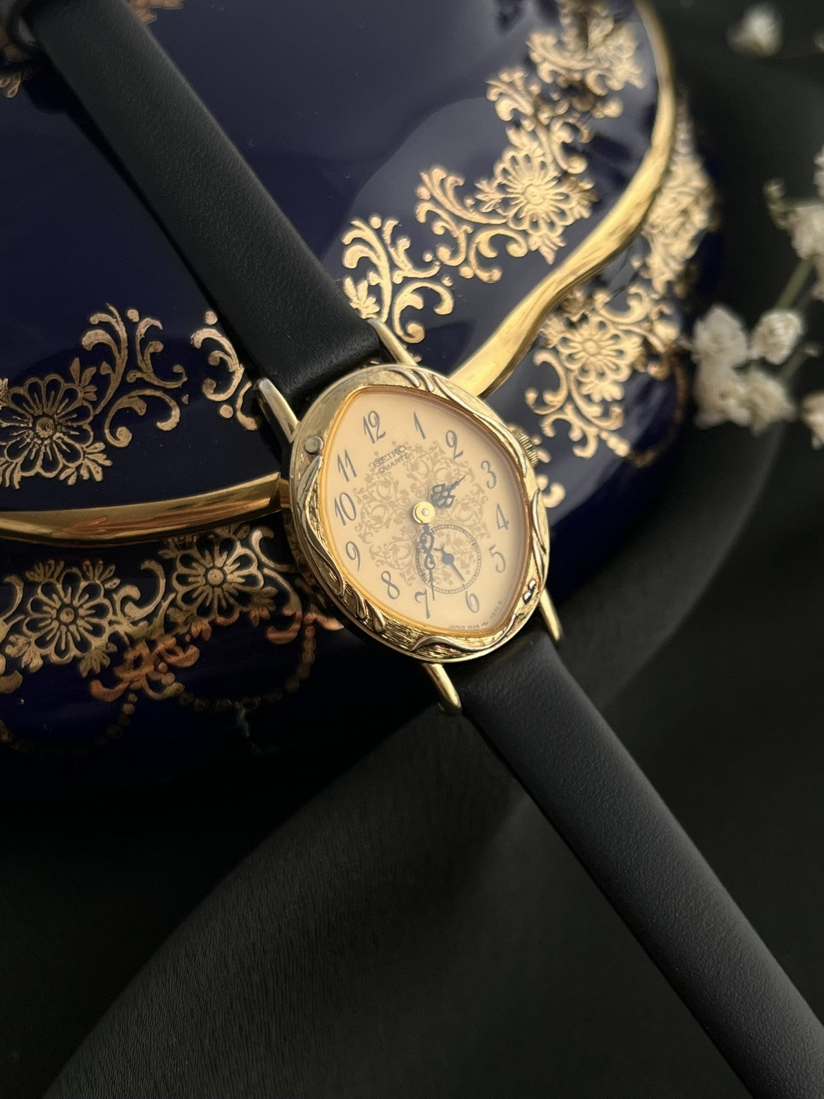Detailed view of the Seiko 1E20-0370 gold-tone case, crown and black leather strap