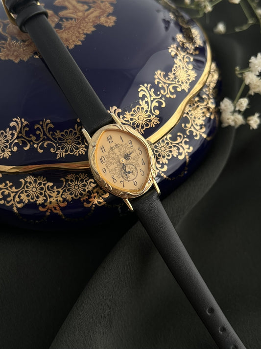 Front view of the Seiko 1E20-0370 gold-tone quartz watch with ornate champagne dial and black leather strap