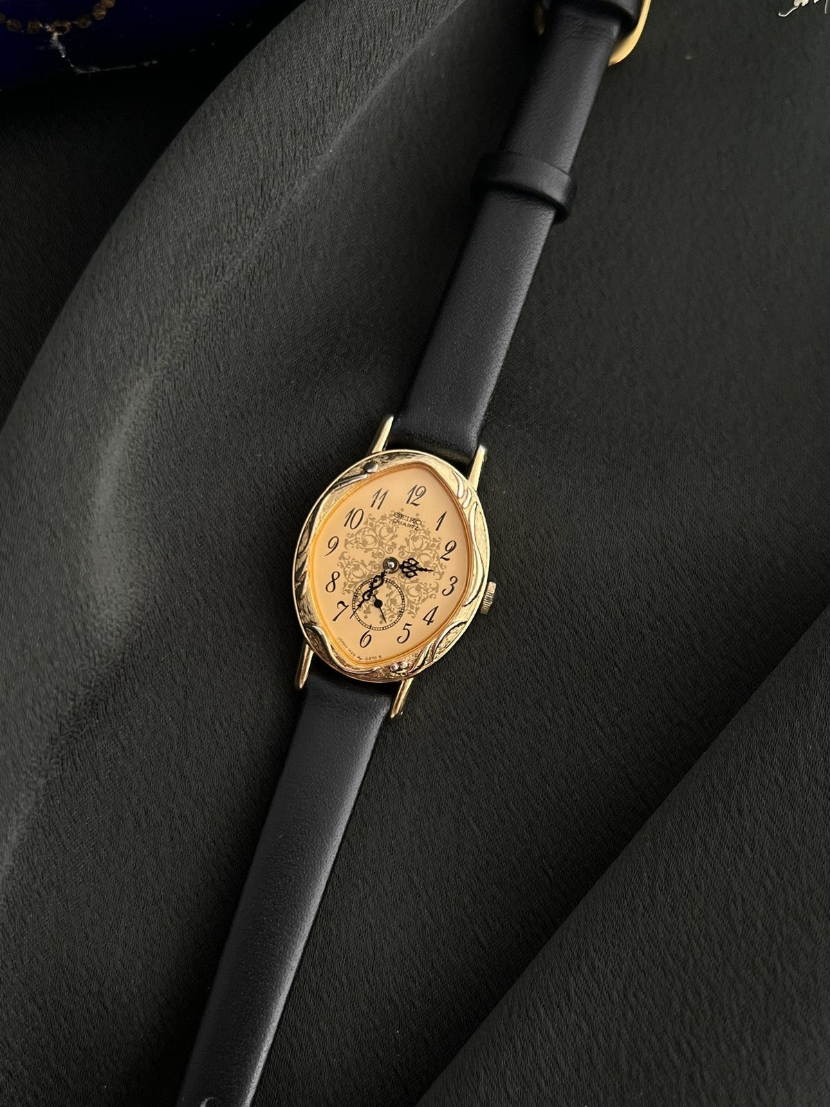 Three-quarter view of the Seiko 1E20-0370 gold-tone watch showing its ornate case and patterned dial