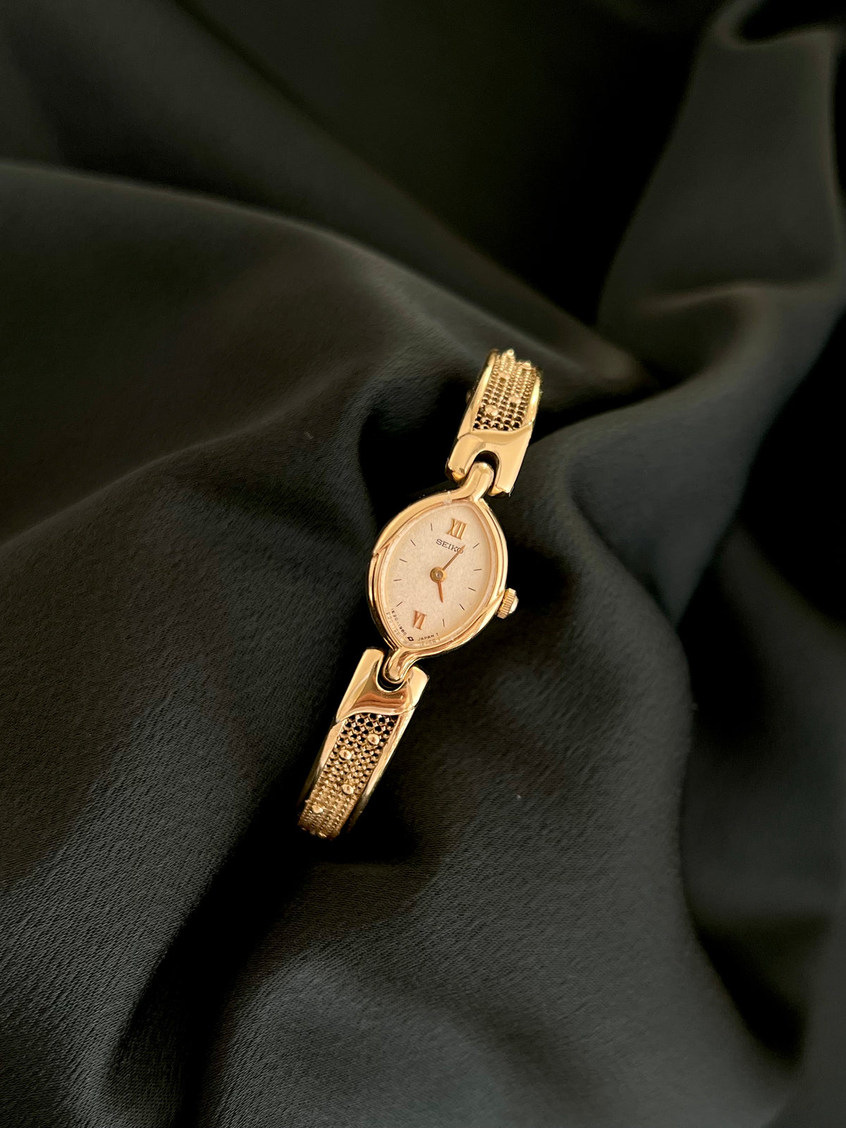 Seiko petite gold-tone oval quartz watch with textured bracelet, front view