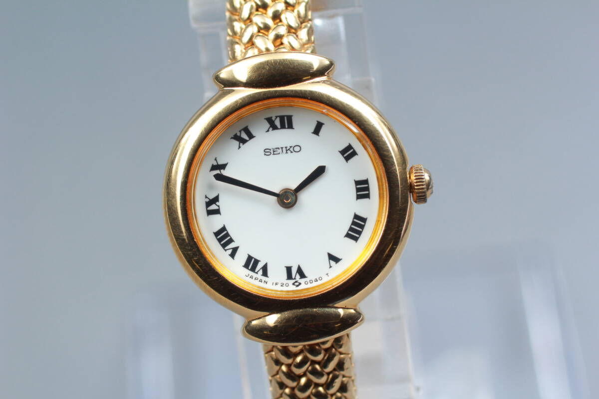 Front view of the Seiko 1F20-0A40 with white Roman numeral dial and gold-tone bracelet