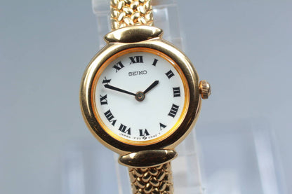 Front view of the Seiko 1F20-0A40 with white Roman numeral dial and gold-tone bracelet