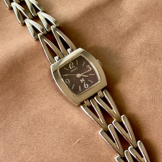 Seiko women’s watch with a deep brown rectangular dial and sculpted linked metal bracelet.