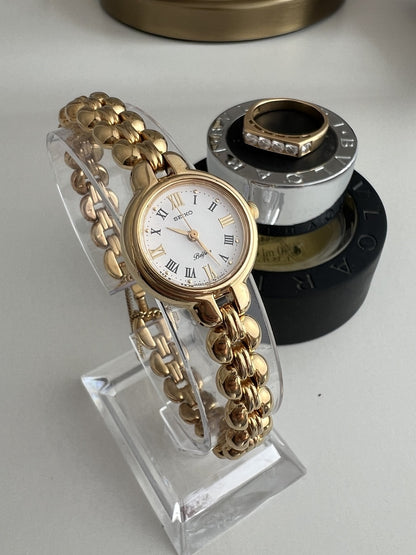 Close view of the Seiko Belfina white dial with black and gold Roman numerals, gold hands and rounded bracelet links.