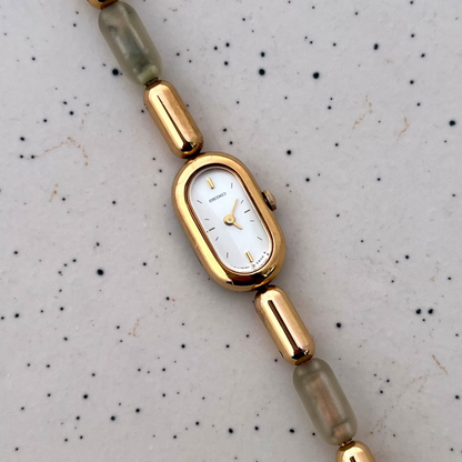 Front view of the Seiko capsule watch with a white dial and gold and translucent resin bracelet.