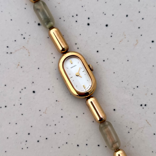 Front view of the Seiko capsule watch with a white dial and gold and translucent resin bracelet.