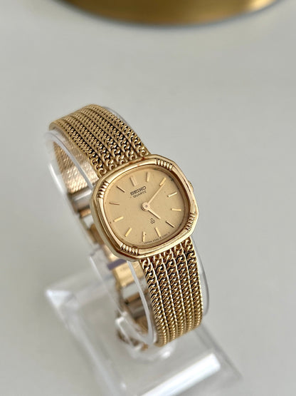 Angled view of Seiko champagne dial, grooved cushion case and interlocking gold tone bracelet