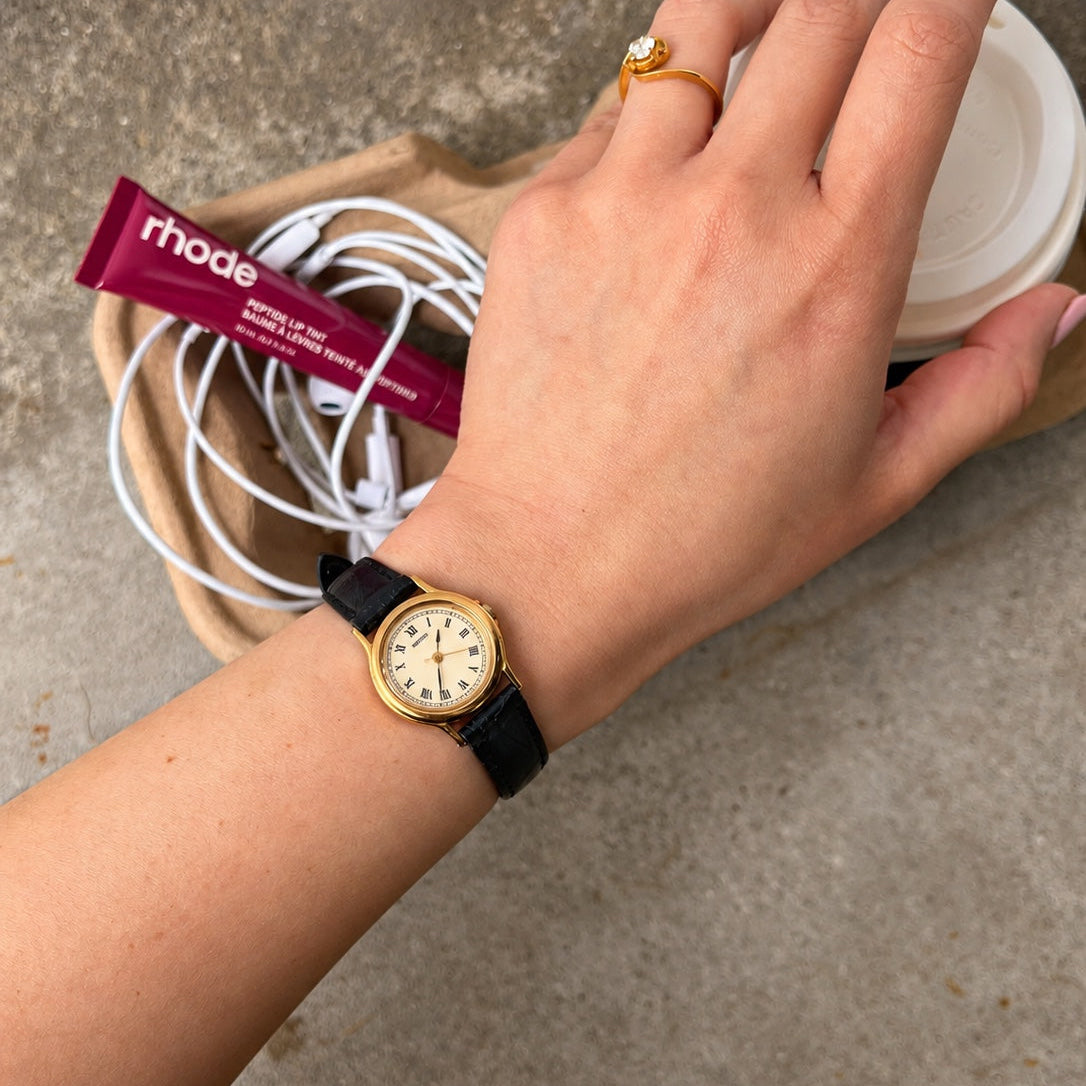 Seiko cream Roman dial women's watch on wrist with a gold tone round case and black leather strap.