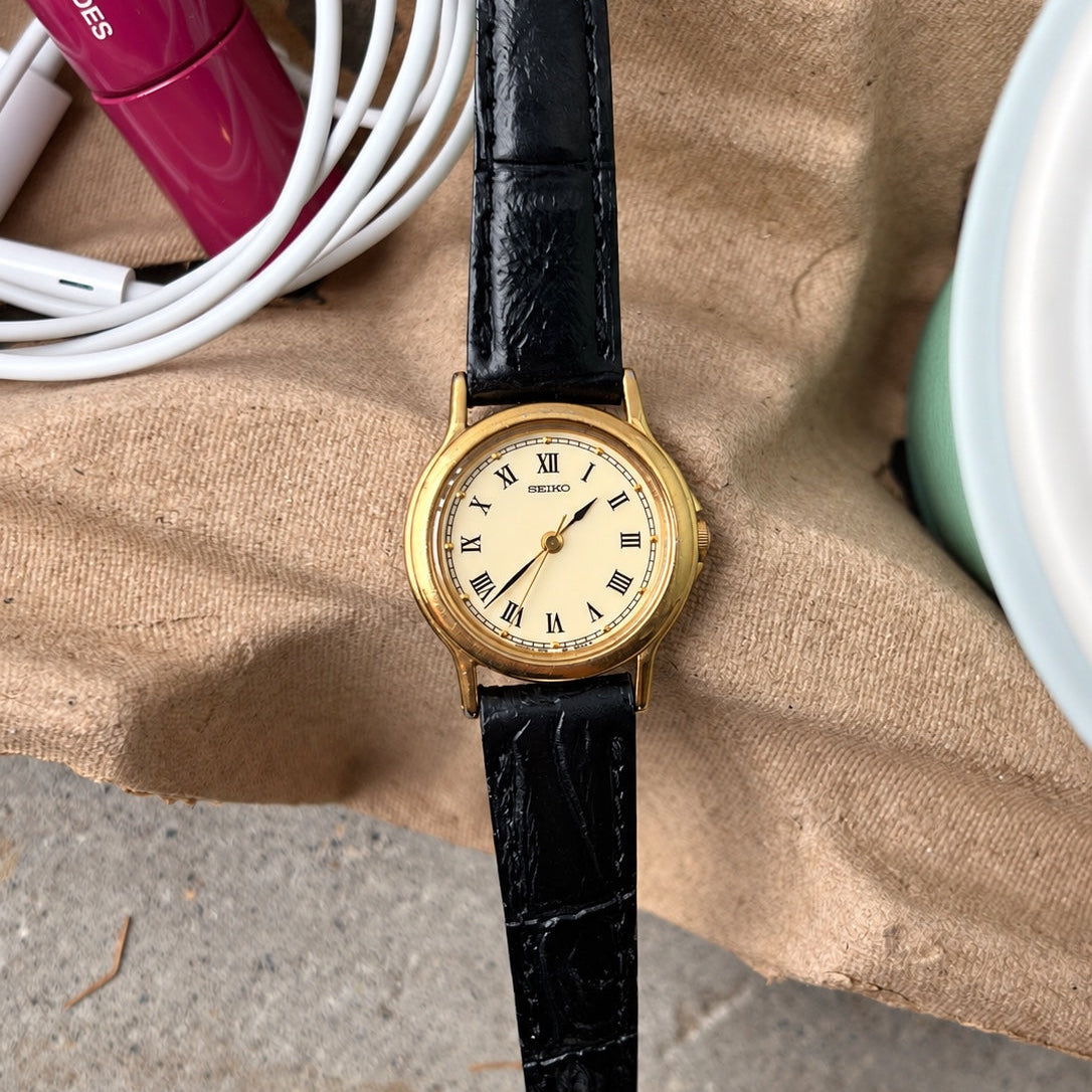 Seiko cream Roman dial, dark leaf shaped hands and gold tone round case with a black leather strap.