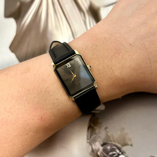 Seiko Exceline women’s watch with black dial, gold rectangular case, Roman numeral detail and black leather strap worn on wrist