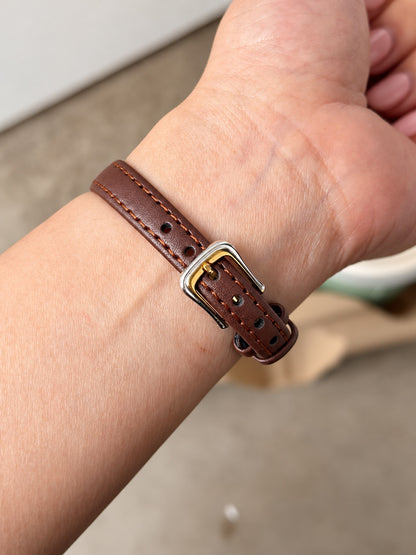 Brown leather strap with contrast stitching, adjustment holes, two keepers and two tone pin buckle on wrist.