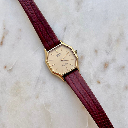 Seiko Exceline gold women’s watch with octagonal case, champagne dial and red lizard grain strap on marble.