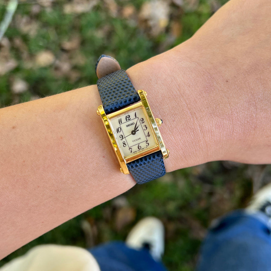 Gold rectangular Seiko Exceline tank watch with blue strap worn on the wrist
