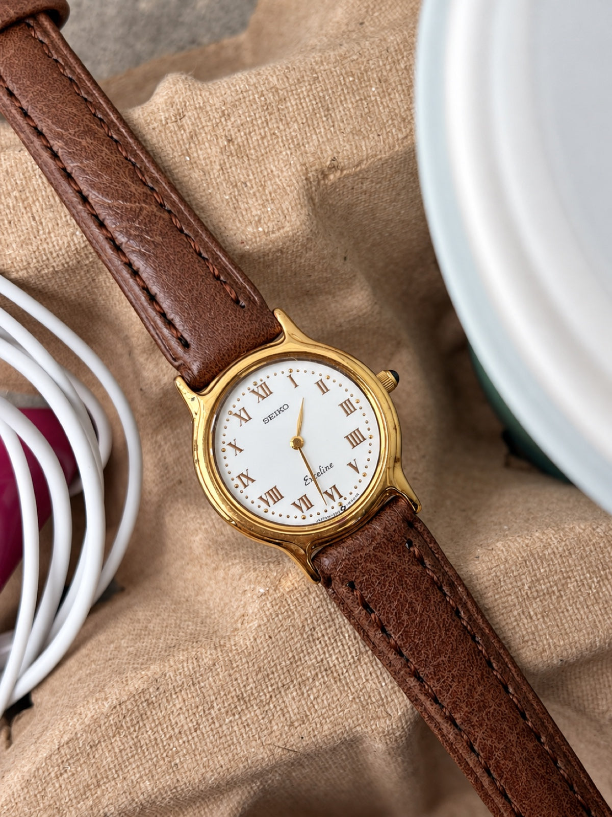 Detail of the Seiko Exceline white Roman dial, gold tone bezel, curved lugs and dark crown stone.
