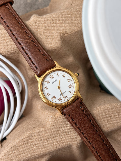 Detail of the Seiko Exceline white Roman dial, gold tone bezel, curved lugs and dark crown stone.