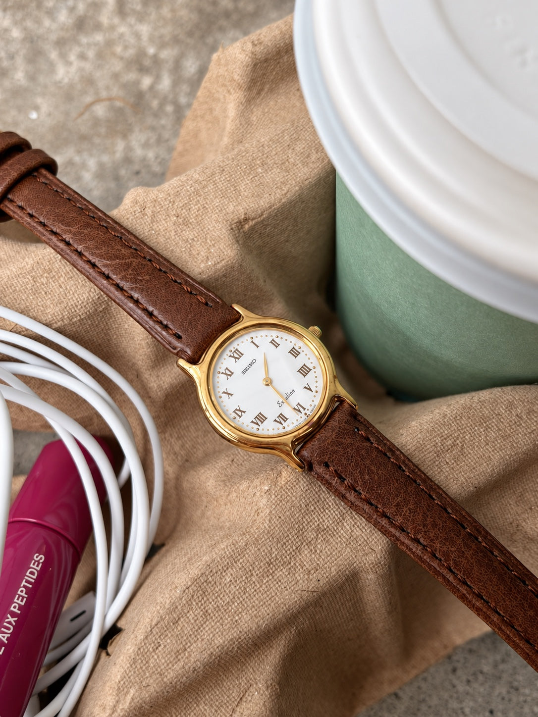 Seiko Exceline gold tone round watch and brown leather strap laid on a neutral fabric surface.